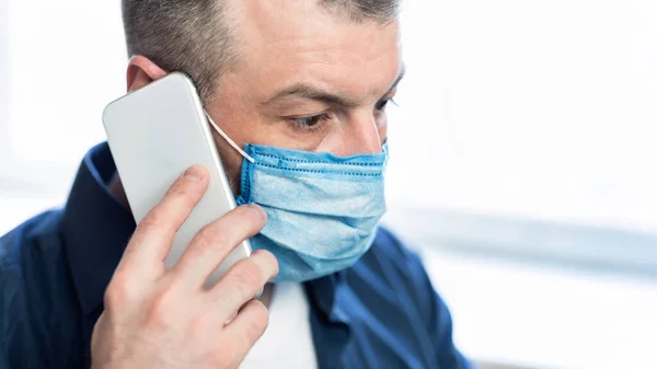 Mężczyzna rozmawiający przez telefon noszący ochronną maskę medyczną w domu — Zdjęcie stockowe
