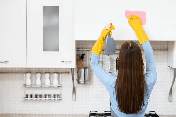 Νεαρή γυναίκα καθαρίζει έπιπλα κουζίνας χρησιμοποιώντας σπρέι και κουρέλι — Φωτογραφία Αρχείου