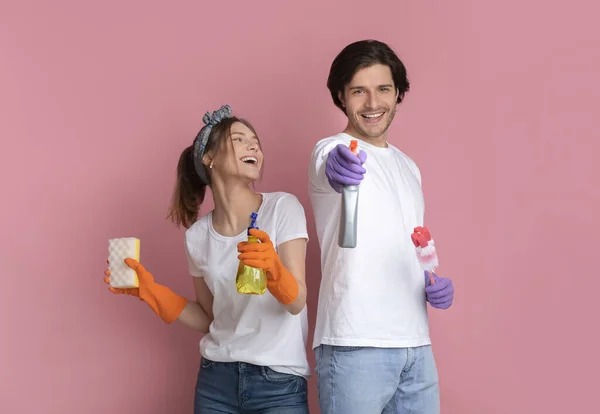 Gioiosa coppia millenaria in posa con prodotti per la pulizia su sfondo rosa — Foto Stock