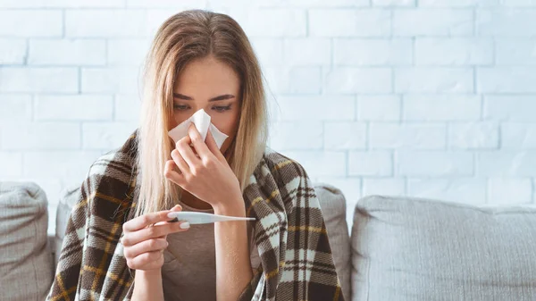 女人看着温度计，用餐巾擦拭鼻子 — 图库照片