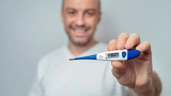 Gezonde man toont thermometer met normale temperatuur over grijze achtergrond — Stockfoto