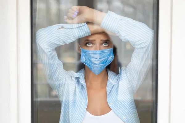 Vrouw met een beschermend masker die thuis uit het raam kijkt — Stockfoto
