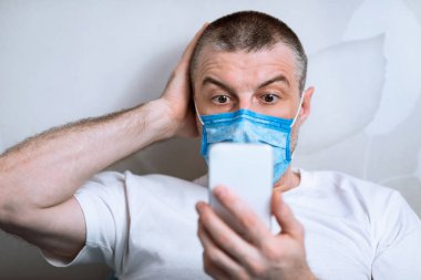 Maskeli Korkak Adam evde oturan telefonu kullanıyor.