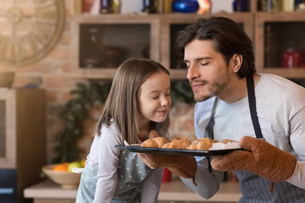 Házi sütemény. Aranyos kislány és apa friss croissant illatot éreznek. — Stock Fotó