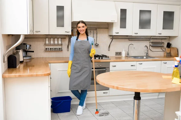 Mujer joven sosteniendo fregona de pie en la cocina —  Fotos de Stock