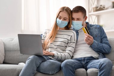 Koruyucu maskeli genç çift internetten alışveriş yapıyor.