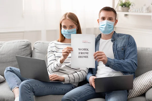 Young couple working online on laptops and holding poster — Stock Photo, Image