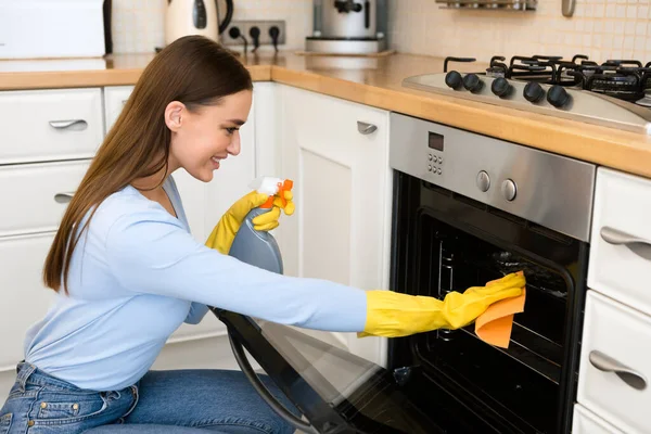 Mujer feliz limpiando muebles de cocina usando spray y trapo —  Fotos de Stock