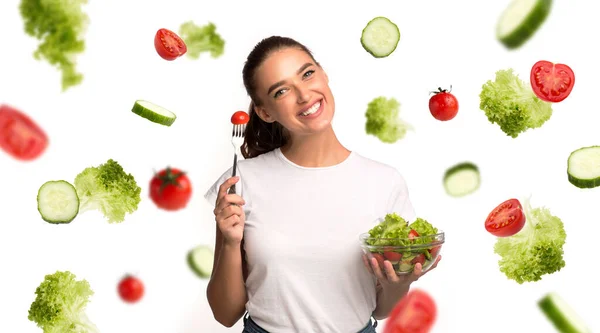 健康饮食。快乐的女孩吃着碗里的沙拉，空气中夹杂着蔬菜，白色背景。全景 — 图库照片