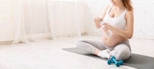 Jovem grávida bebendo água sentada em posição de lótus — Fotografia de Stock