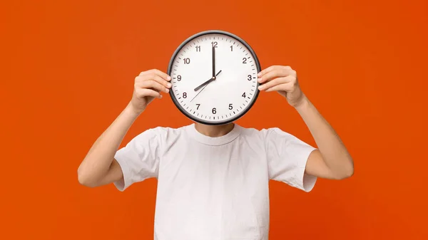 Adolescente menino cobrindo seu rosto com grande relógio, panorama laranja — Fotografia de Stock