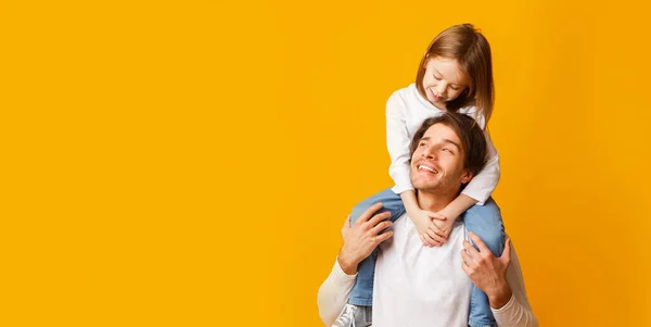 Preschool girl sitting on father shoulders over yellow background — Stock Photo, Image