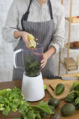 Tanınmayan bir kadın taze yeşilliklerle smoothie yapıyor.