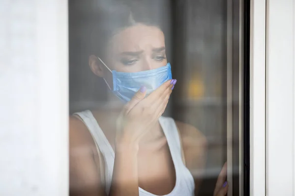 Zieke vrouw hoesten dragen masker Kijken door het raam thuis — Stockfoto