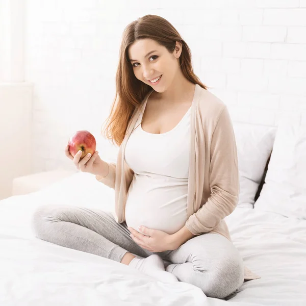 Wanita hamil makan apel di tempat tidur di rumah — Stok Foto