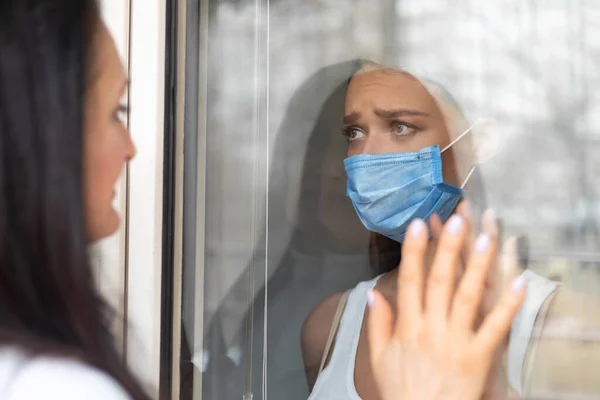 Ongelukkig meisje aanraken moeders hand door glazen deur thuis — Stockfoto