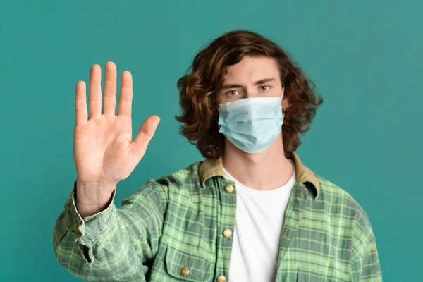 Молодой парень в медицинской маске и показывает жест СТОП, бирюзовый фон — стоковое фото