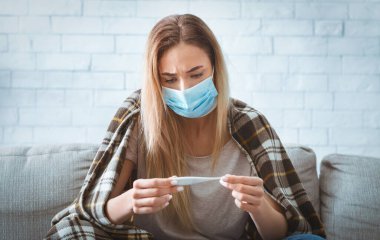 Kanepedeki hasta kadın termometreye bakıyor.