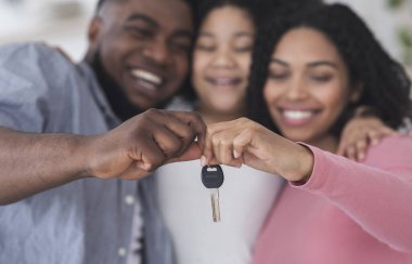 Üç kişilik gülümseyen siyah aile yeni evlerinin anahtarlarını tutuyor.