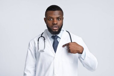 Kafası karışmış beyaz üniformalı erkek doktor kendini işaret ediyor.