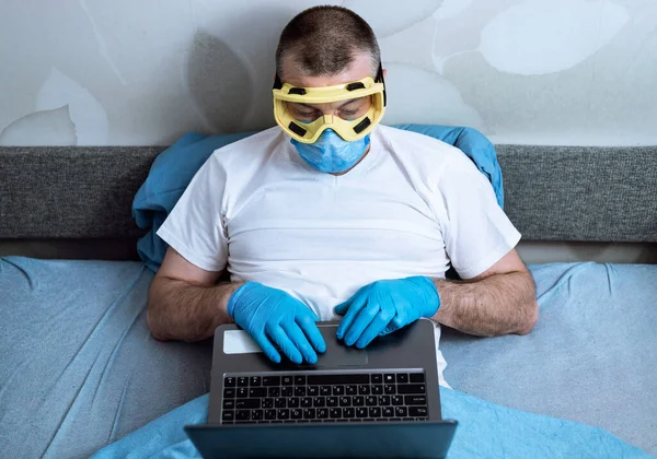 Mężczyzna pracujący na laptopie w masce i rękawiczkach w domu — Zdjęcie stockowe
