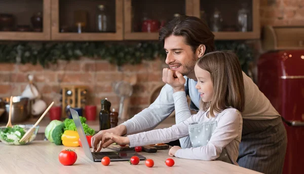 Giovane papà e sua figlia leggono la ricetta sul computer portatile in cucina — Foto Stock