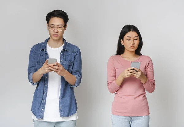 Couple asiatique debout à part et en utilisant des téléphones mobiles — Photo