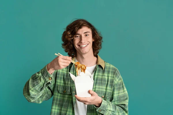 Comida Takeaway. Happy millennial cara comendo macarrão chinês de caixa descartável, fundo turquesa. Espaço vazio. — Fotografia de Stock