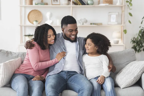 Amoroso negro hombre abrazando esposa e hija en sofá en casa — Foto de Stock