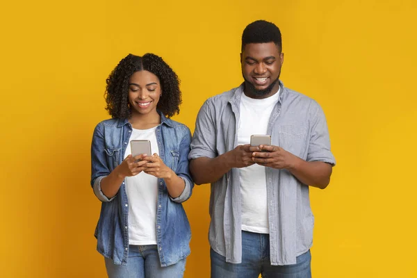 Pasangan kulit hitam yang bahagia sibuk dengan smartphone mereka, SMS atau browsing internet — Stok Foto