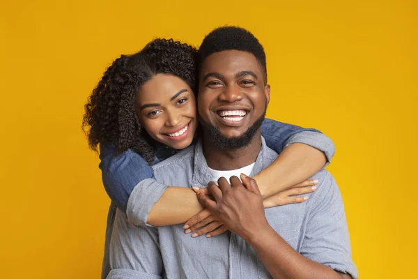 Szczęśliwi razem. Rodzinny portret uśmiechniętej czarnej pary przytulającej, żółte tło — Zdjęcie stockowe