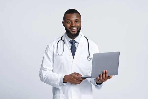 Dost canlısı Afrikalı doktor dizüstü bilgisayarını beyaz arka planda tutuyor. — Stok fotoğraf