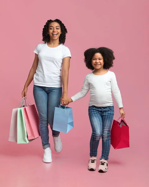 Alegre mujer negra y su linda hija caminando con bolsas de compras —  Fotos de Stock