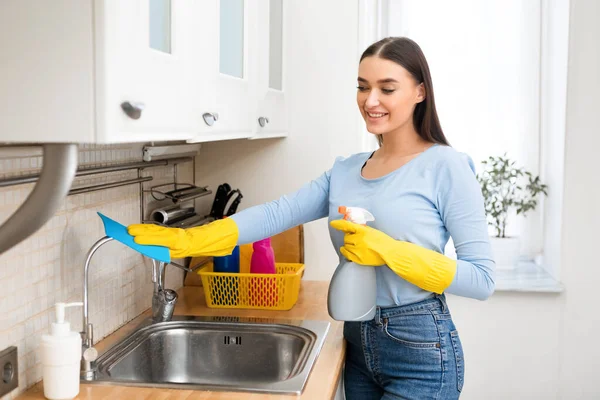 Mulher sorrindo limpeza de móveis de cozinha usando spray — Fotografia de Stock