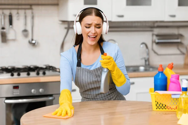 Giovane donna con cuffie pulizia tavolo da cucina — Foto Stock