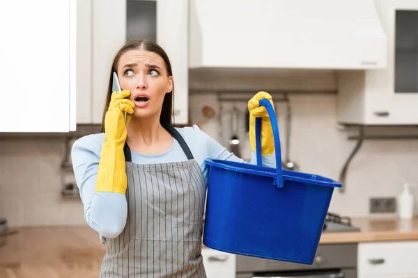 Mujer joven asustada llamando a fontanero sosteniendo cubo — Foto de Stock