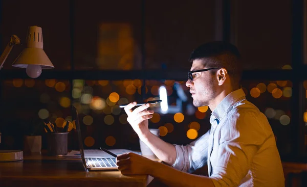 Σοβαρός επιχειρηματίας που χρησιμοποιεί Voice Assistant κάθεται στο γραφείο τη νύχτα — Φωτογραφία Αρχείου