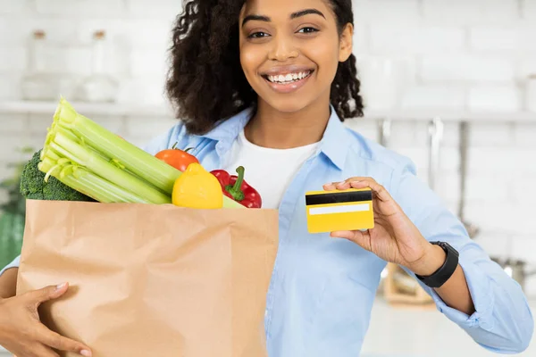 Афро девушка показывает кредитную карту и бумажный пакет с едой — стоковое фото