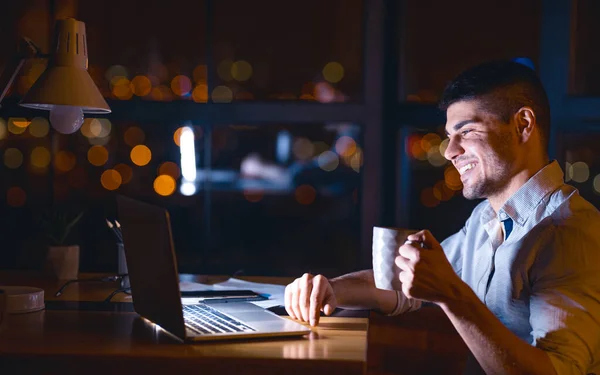 Homem no computador portátil tendo café trabalhando durante a noite no escritório — Fotografia de Stock