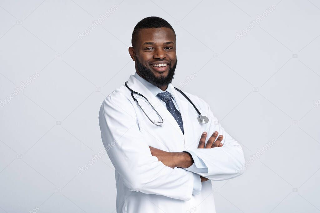 Confident black doctor posing over white studio background