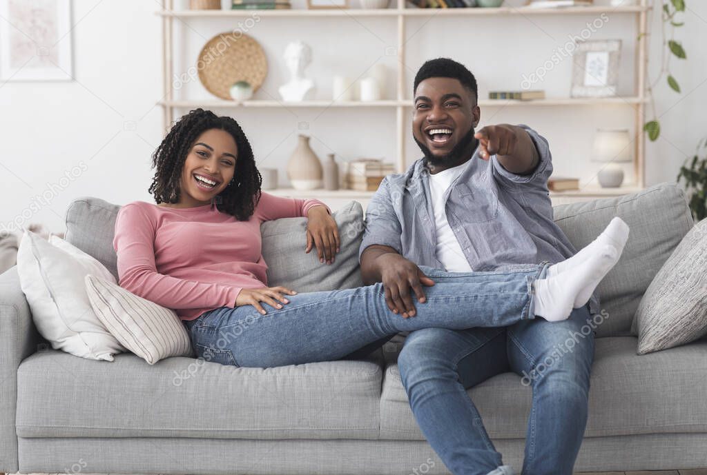 Cheerful black couple watching comedy movie on tv and laughing