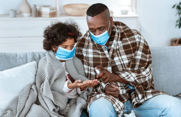 Estrategias de higiene epidémica. Familia afroamericana con máscaras protectoras y manos limpias con desinfectante en interiores —  Fotos de Stock