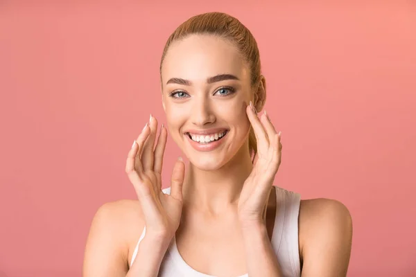 Ragazza allegra che tocca il viso sorridendo alla macchina fotografica, sfondo rosa dello studio — Foto Stock