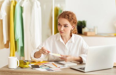 Kadın moda tasarımcısı elinde renk örnekleri ile masada oturuyor.