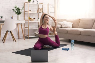 Kişisel izolasyon sırasında spor. Çekici kız çevrimiçi eğitim sınıfını izliyor ve evde yoga yapıyor.