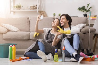 Smiling young couple taking selfie on smartphone after spring-cleaning apartment clipart