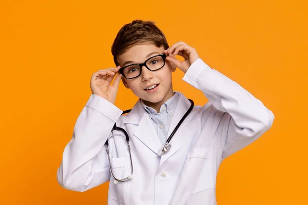 Adolescente brincalhão em uniforme médico posando em fundo laranja — Fotografia de Stock