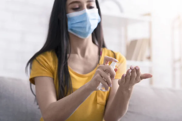 Предотвращение коронавируса. Молодая девушка в медицинской маске наносит дезинфицирующее средство на руки дома — стоковое фото