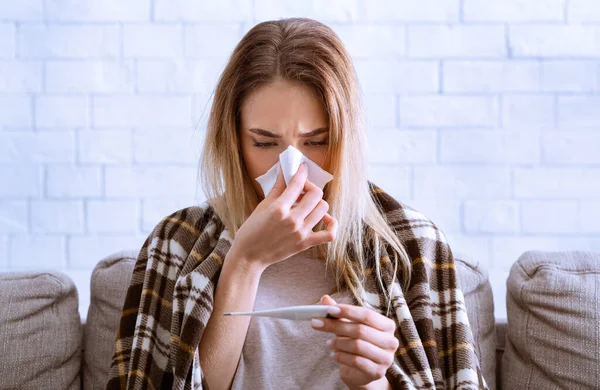 Женщина вытирает нос и смотрит на температуру — стоковое фото