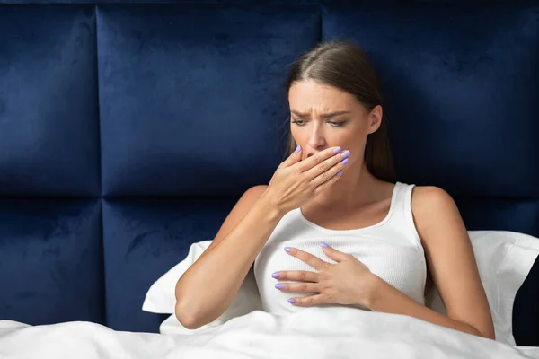 Mujer tosiendo y tocando el pecho sintiéndose mal sentada en la cama — Foto de Stock